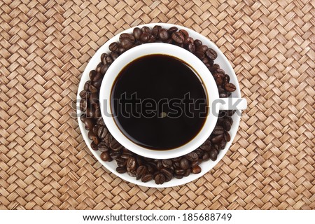 dark coffee with beans in white cup on rattan table background