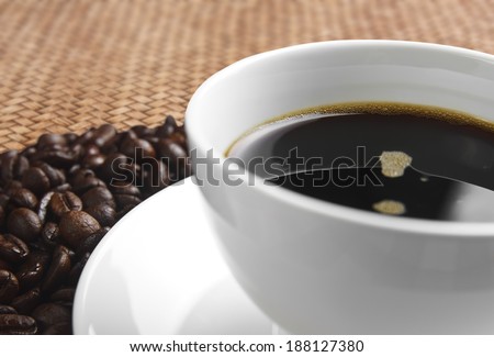 close up dark coffee in white cup with beans on rattan table background
