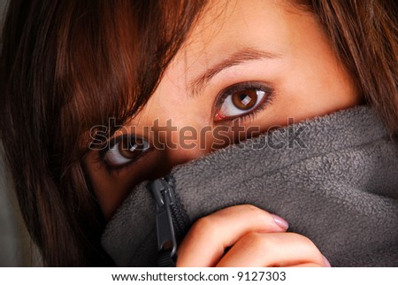 A pretty girl with mysterious eyes with sweater pulled up over face.