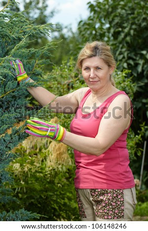 Mature woman works in her garden, wear pink top and colorful gloves