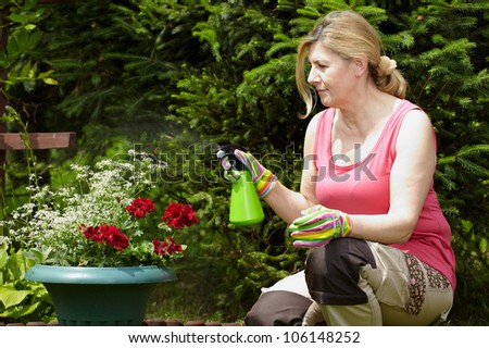 Mature blonde woman works in her garden, spray flowers using green water bottle