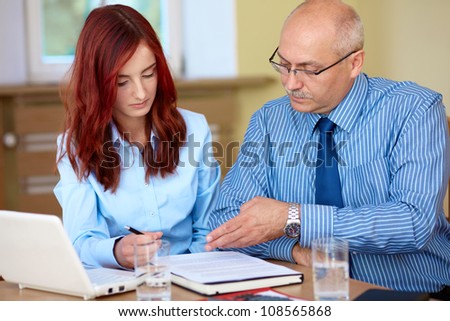 Senior businessman with young redhead female colleague discuss something