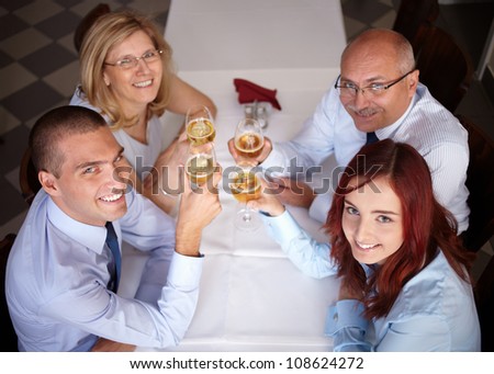 Group of 4 younger and older businesspeople celebrate with wine glasses in their hands