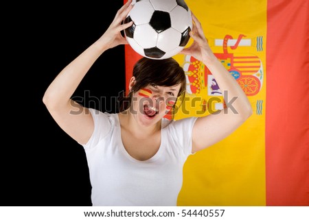 young female, spanish football team supporter with flag as background and small flags on her cheeks, holds football ball over her head, joy, enthusiasm
