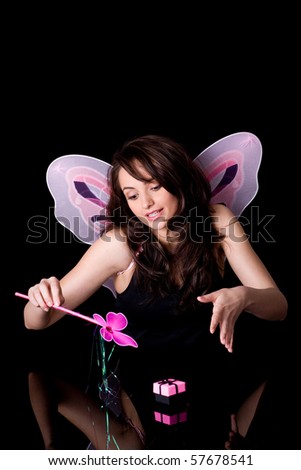 fairy with pink wings and magic wand doing some magic over small gift box, studio shoot isolated on black
