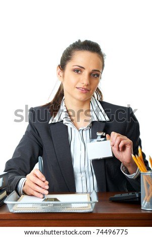young happy female office worker sits at her desk, holds her id badge, isolated on white background