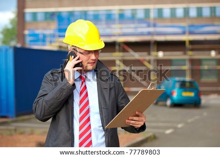 young architect or inspector talk over his mobile phone, outdoor shoot with blurred office building as background