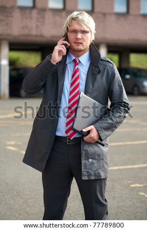 young architect or inspector with office building as blurred background, talks aver his mobile phone