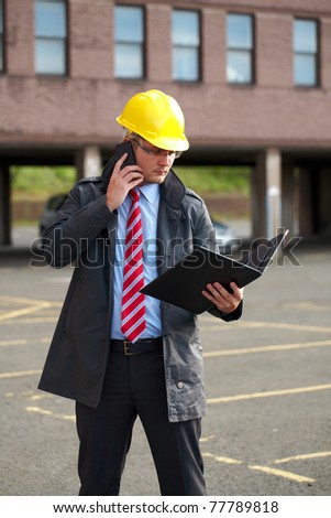 young architect or inspector with office building as blurred background, talks over his mobile phone