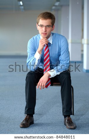 Young thoughtful businessman in blue shirt and red tie, office shoot