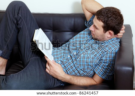Young man sits on black sofa and reads book
