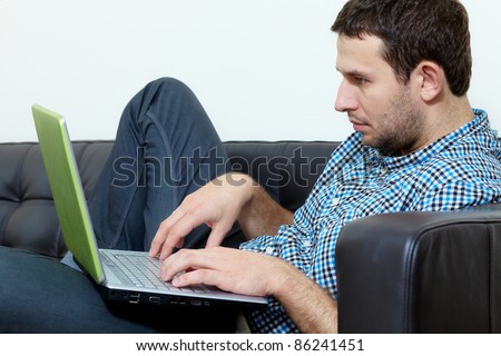 Young man sits on sofa and works on his laptop computer