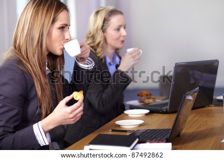 Two businesswoman sitting at conference table have a break during meeting