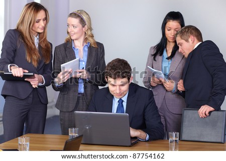 Team of 5 business people behind young businessman sitting and working on his laptop