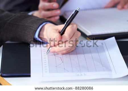 female hand holds pen over graph printed on A4 size document