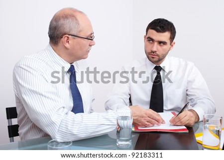Two businessman, one mature and one young sitting at table during meeting