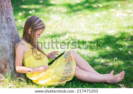 Cute little girl learning with tablet pc in the park