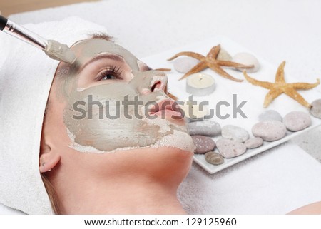 Young beautiful girl receiving clay facial mask in spa beauty salon