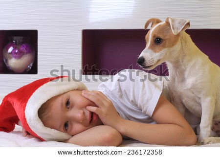 Cute little boy playing with his dog jack Russell terrier and wearing Santa hat