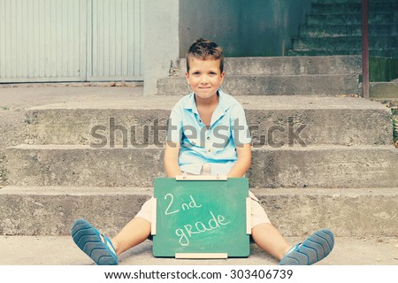 Boy holding Chalkboard with words Second Grade. Outdoor photo