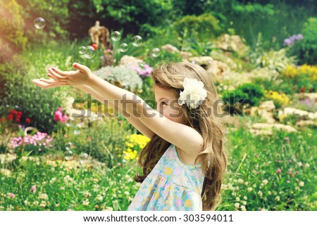Fine art summer portrait of beautiful girl playing outside with soap bubbles
