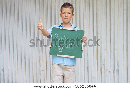 Stylish boy , Schoolboy holding Chalkboard with words second grade, ready for school. Outdoor photo. Education and kids fashion concept