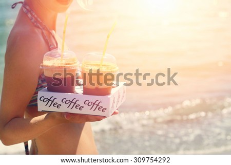 Attractive female waiters holding two ice frappe coffee on the beach near sea, sunset colors