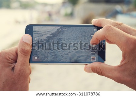 Close up on male hands taking photo of sea coast with mobile cell phone. Summer beach holiday vacation concept