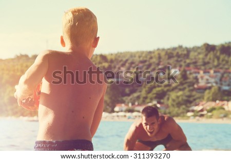 Father and son playing with a ball  on the beach near the sea. Man and boy against ocean, active summer holiday vacation,hazy summer light photo