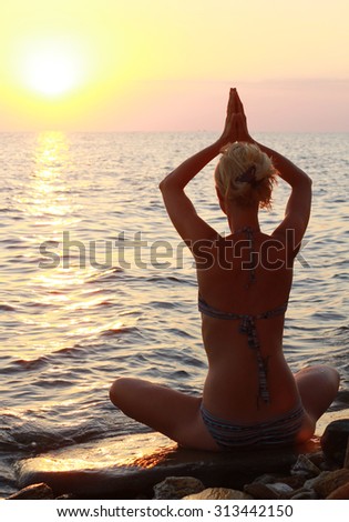 Yoga, woman meditating in lotus pose on the beach near the sea, ocean, during sunset