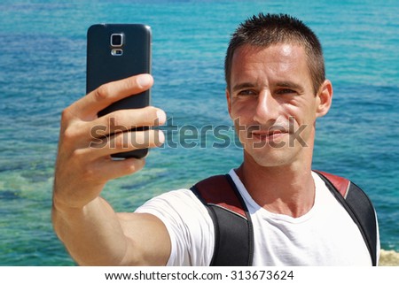 Portrait of young man taking selfie by cell, mobile phone , smartphone on beach near sea, ocean