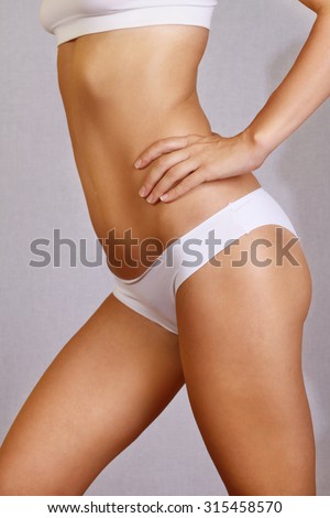 Fitness girl, close up of a young woman showing flat belly, stomach trained buttocks, slim tanned woman\'s body on white background.