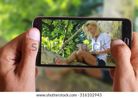 Male hand taking photo of Beautiful young woman using laptop in nature with cell, mobile phone. Freelancer working in a park outdoors.