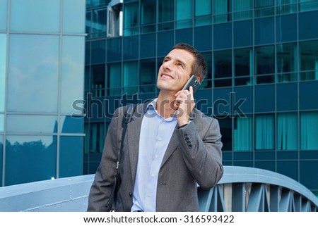 Young handsome, successful businessman, manager talking on the phone in the city, in front of modern building