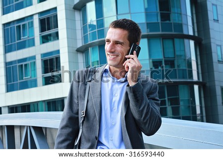 Young handsome, successful businessman, manager talking on the phone in the city, in front of modern building