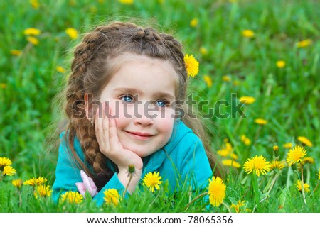 a cute little girl dreaming on green grass with lots of dandelions