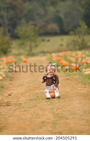 Cute Smiling Infant Baby Girl Sitting on a Pumpkin in a Pumpkin Patch. Her knees are dirty because she\'s been crawling and playing with pumpkins. Taken near Chattanooga Tennessee on October 27, 2013.