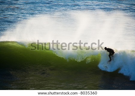Shot of a surfer on a wave as the wind creates spray off the top of the wave.