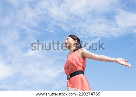 Young woman spreading arms on sky background.
