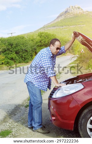 Adult man is standing near his broken car waiting for tow