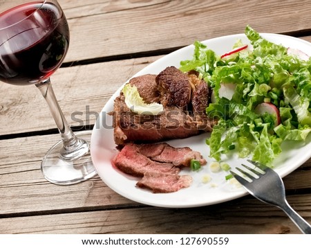 Veal meat with green salad with a red wine glass, horizontal view