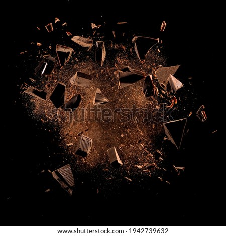 Cocoa powder with chocolate pieces and curls explosion on black backgrounds
