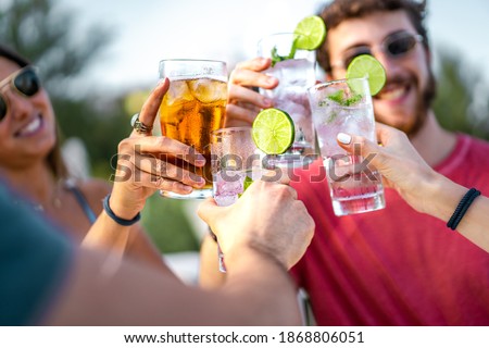 Happy young friends toasting with mojito cocktails together. Focus on the glasses clinking. Friendship and alcohol abuse concept.
