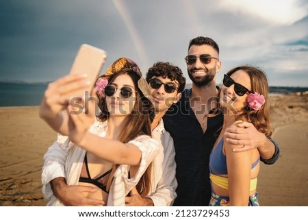 Best friends carefree on the beach after the rain taking a selfie with the rainbow in the background - happy young people smiling watching the phone camera together 商業照片 © 