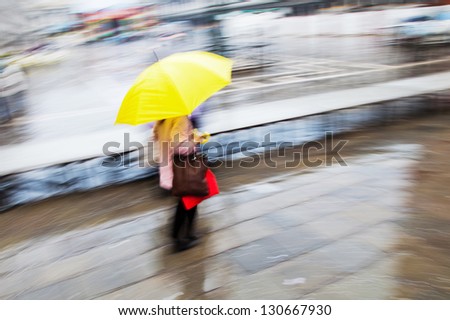picture in motion blur of a woman with a yellow umbrella on the move in the city