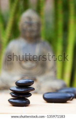pile of massage stones on a bamboo mat with a buddha statue and bamboo in the blurred background
