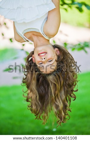pretty young girl hangs down from a tree, smiles, and her long hairs hanging down