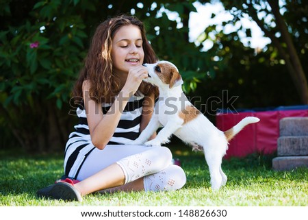 happy young girl plays with a cute Parson Russell Terrier puppy in the garden