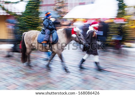 woman leading a pony with a child on a christmas market in motion blur
