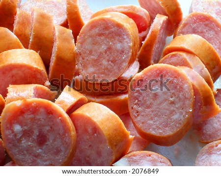 Sliced smoked sausage on a white cutting board, ready to be cooked.